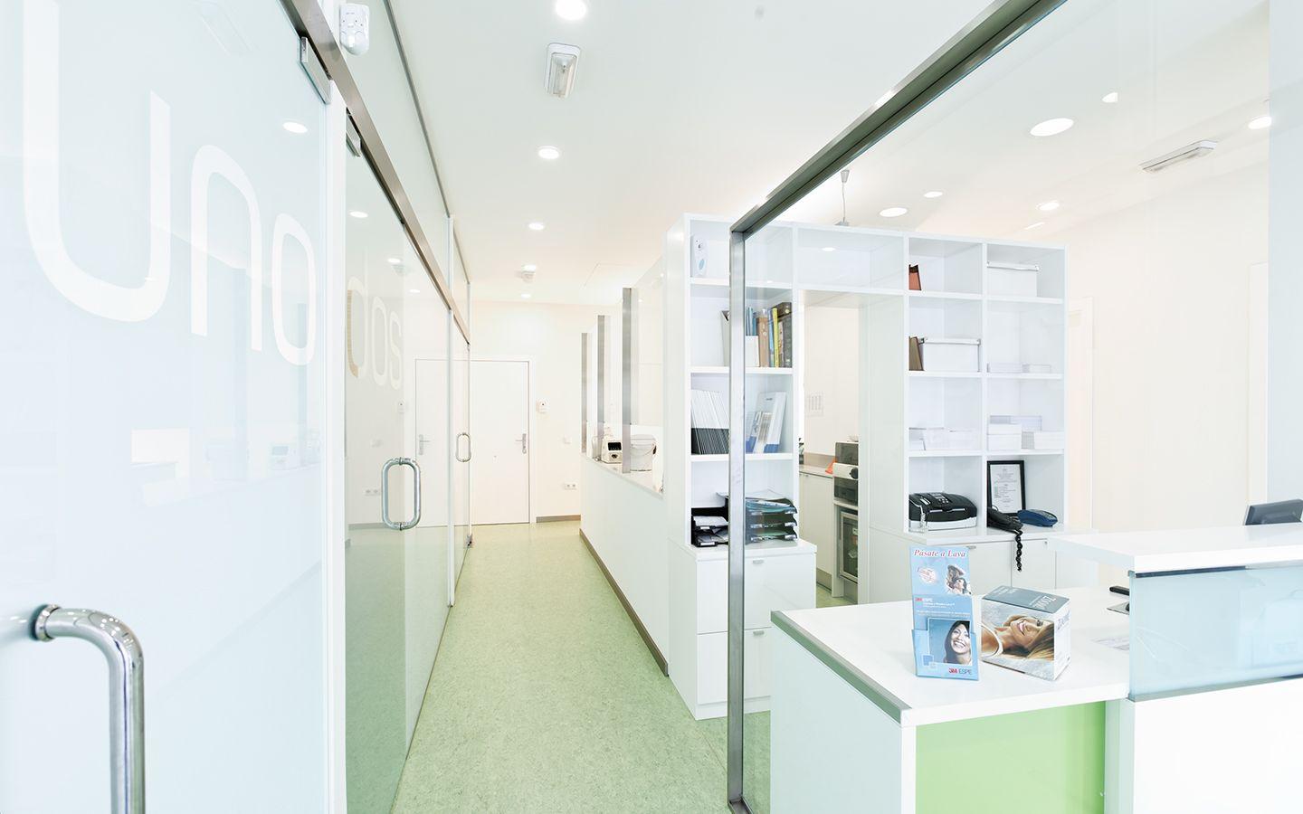 Bright and modern dental office with glass partitions, white shelves, and reception area.