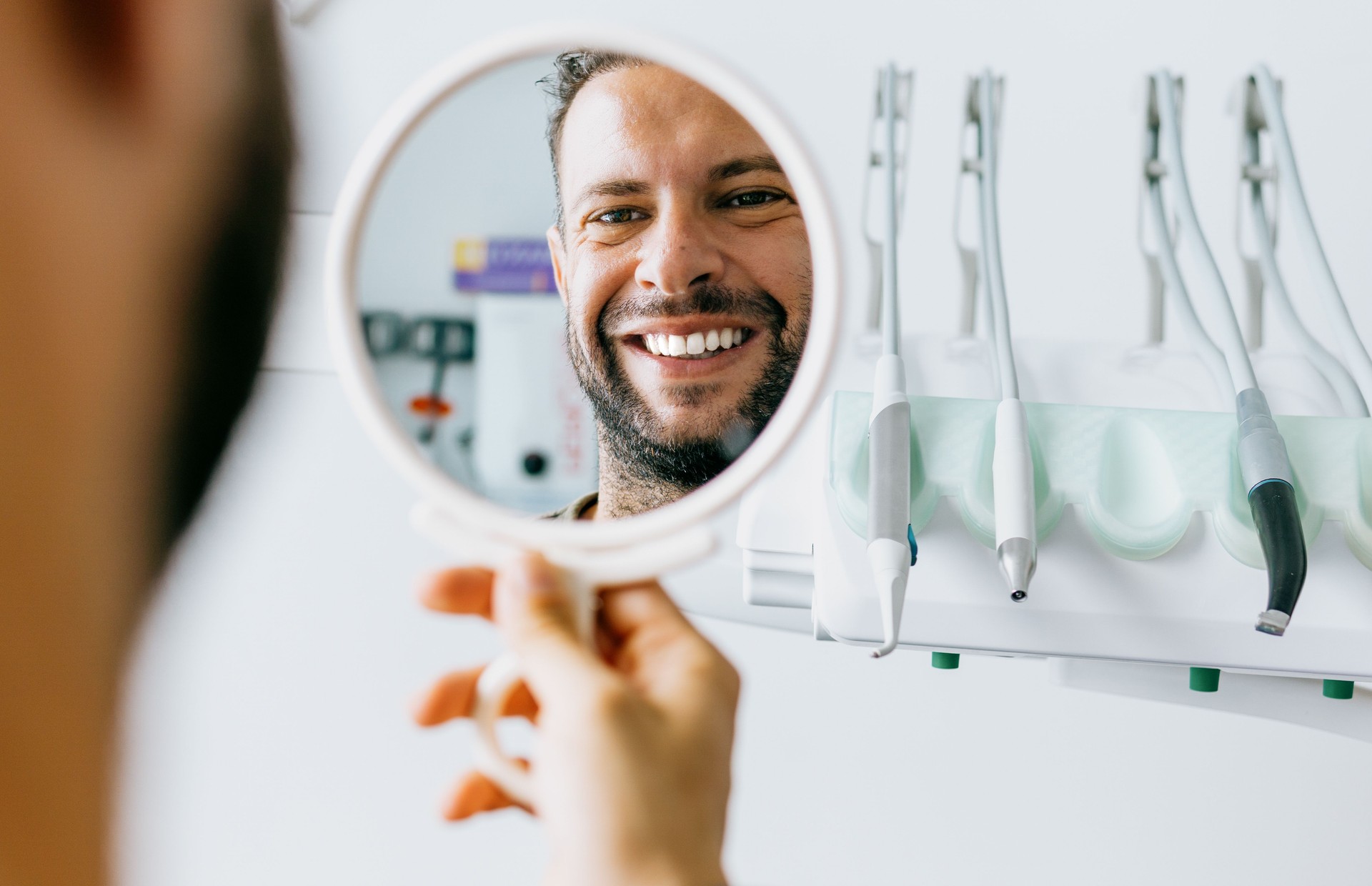 El hombre satisfecho se mira en el espejo y sonríe después del tratamiento en el dentista